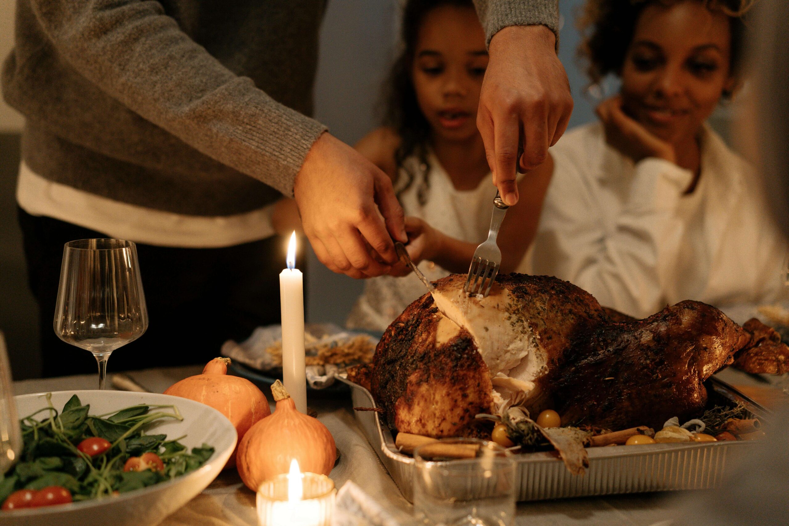 Dad carving a turkey with mom and daughter looking on with candle on the table